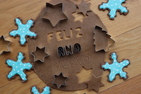 Feliz ano nuevo . Gingerbread Cookie dough letters on wooden table with festive cookie cutters and glazed cookies