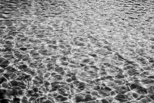 Black and white water texture with clear sun glare, light ripples on the water surface