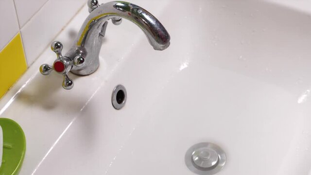 Close-up of a man's hand opening the plug in the sink drain and water going down the drain