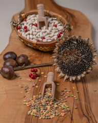 Colorful lentils on a wooden cutting board with a dry sunflower and white beans on the background