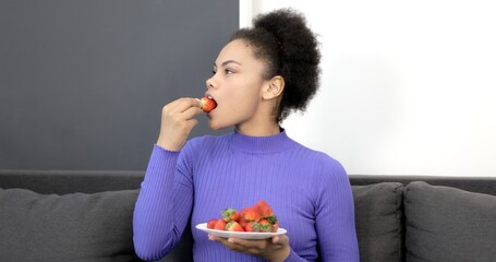 Hungry African American woman eating strawberries from a bowl. The black woman illumines with berries. Healthy eating.