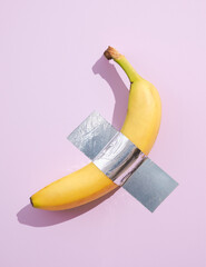 Ripe banana glued with silver tape to pink wall. Bright and sunny idea summer.