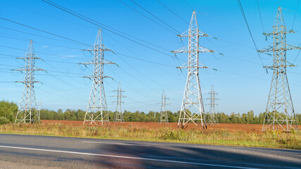 High-voltage power lines and power pylons near the highway. Transmission towers in industrial landscape. High voltage electric transmission towers.