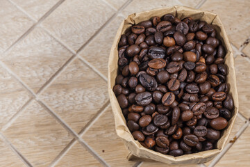 Coffee beans in a brown paper bag on wooden background.