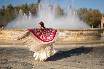 Young flamenco woman, Hispanic and brunette, with typical flamenco dance suit, dancing with red...