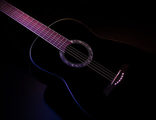 Fototapeta na wymiar black guitar against split colored dark background. guitar music low-key concept