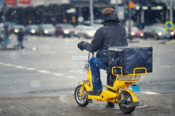 Winter food deliver service. Man on electric moto bike, deliver food orders to customers during...