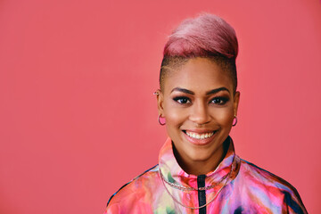 Portrait of a happy stylish young woman with pink hair and colofrful fashion jacket on pink...