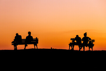 Fototapeta na wymiar on a hot summer day at sunset people sit on a bench discussing affairs and plans silhouettes of people