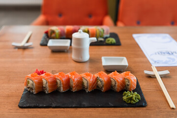black plates with tasty sushi rolls near chopsticks, soy sauce pot and blurred menu on wooden table