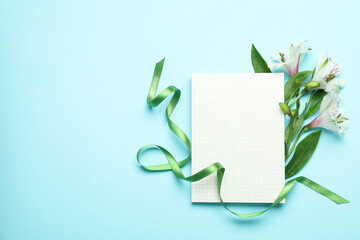 Lilies, green ribbon and blank sheet on blue background
