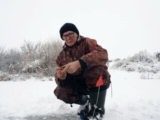 Fototapeta na wymiar Winter fishing. A fisherman sits on a frozen river and catches fish in a drilled hole, an ice hole.