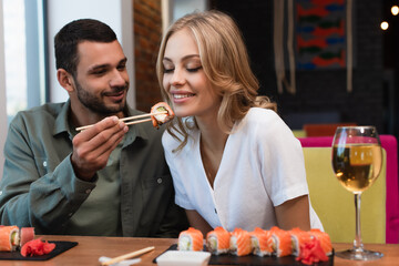 young man feeding happy woman with sushi roll during dinner in restaurant