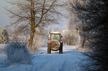 Traktor na zimowej polnej drodze z balotem siana - 477433075