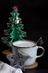 a mug of coffee with milk and wooden Christmas toys: a green Christmas tree a brown star, next to a...