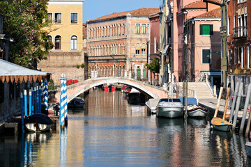 Fototapeta na wymiar Venice in Italy with footbridge across canal with reflection. Old houses. Romantic old architecture. Boats and pedestrian bridge over canal.