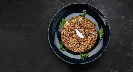 Buckwheat porridge with butter and herbs on a plate, on a dark background