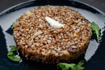 Buckwheat porridge with butter and herbs on a plate, on a dark background