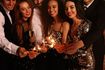 Happy friends with glasses of sparkling wine and sparklers celebrating New Year, focus on hands