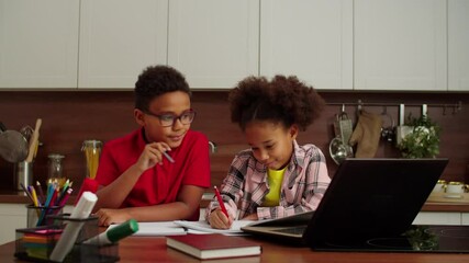 Cute smart school age African American boy in eyeglasses and cheerful younger sister doing homework together, learning online using laptop pc while siblings studying in domestic interior. - Powered by Adobe