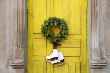 Pair of ice skates and Christmas wreath hanging on old yellow door