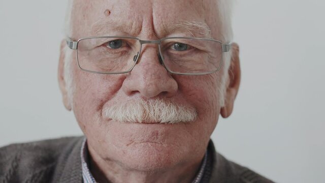 Slowmo close up portrait of Caucasian senior man with grey moustache in eyeglasses smiling at camera on white background