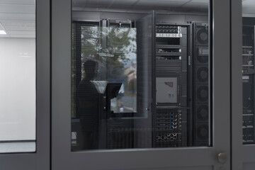 Software Engineer Working on a Laptop Computer in a Modern Server room. Monitoring Room Big Data Scientist in reflection of the entrance door.