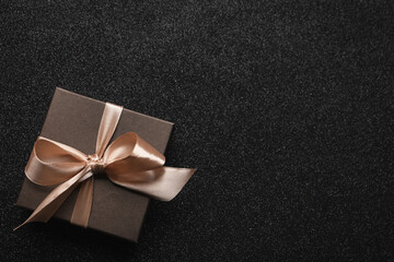 Gift box with golden bow on black background, top view. Space for text