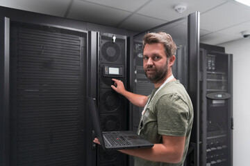 Fototapeta na wymiar Data Center Engineer Using Laptop Computer Server Room Specialist Facility with Male System Administrator Working with Data Protection Network for Cyber Security or Cryptocurrency Mining Farm. 