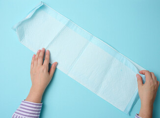 female hand holds a disposable medical diaper on a blue background. Hygiene product