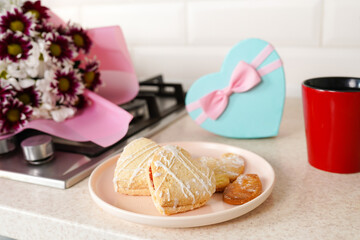 Heart cookies on plate on light kitchen table with flowers and gift box for Valentine's Day