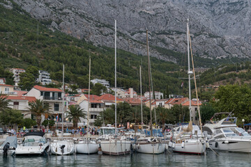 Fototapeta na wymiar Moored sailing ships in Adriatic sea in marina in touristic resort Baska Voda, Croatia against mountain Biokovo