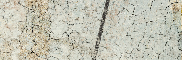 Peeling paint on the wall. Panorama of a concrete wall with old cracked flaking paint. Weathered rough painted surface with patterns of cracks and peeling. Wide panoramic grungy texture for background