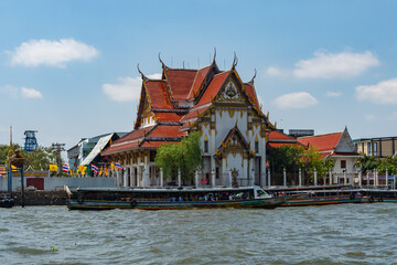 Boat on the Chao Phraya River in front of the Buddhist temple Wat Rakhangkhositaram, Bangkok, Thailand.