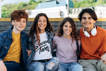 Positive, cute teenagers sit on a bench, look at the camera, smile. Cute boys and girls, schoolchildren outdoors
