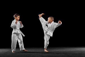 Two little kids, boys, taekwondo athletes training together isolated over dark background. Concept of sport, education, skills © master1305