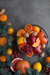 Naklejka na ściany i meble Many different seasonal fruits and walnuts in a plate on a beige table. Background with nuts, tangerines, pomegranates, grapefruits, persimmons and lemons