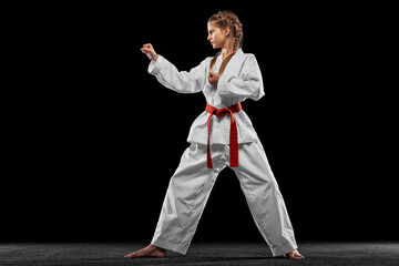 One young girl, teen, taekwondo athlete posing isolated over dark background. Concept of sport,...