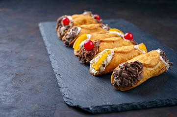 Traditional Italian Sicilian pastry dessert cannoli with creamy ricotta filling, chocolate crisps and fresh currant fruit served as close-up on a rustic black board