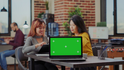 Colleagues working on business investment with green screen on laptop in office. Team of women using computer with isolated copy space and chroma key template for mockup. Blank background