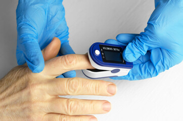 Saturation measurement of a 60-year-old Asian woman. The hands of a doctor in medical gloves apply a pulse oximeter to the finger of an elderly woman. Caring for the health of the elderly
