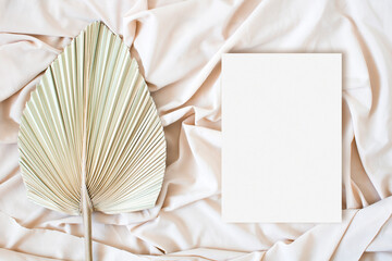 Top view mockup wedding card with leaf palm on the nude fabric
