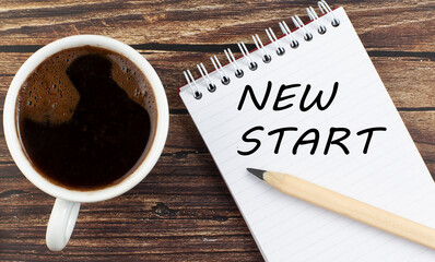 NEW START text on notebook with coffee on wooden background
