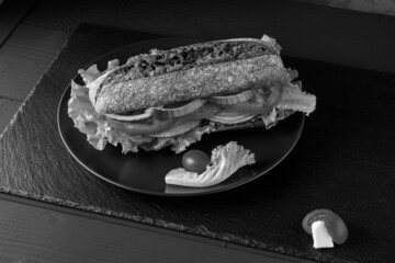 Breakfast tomato sandwich with salad on black stone background.