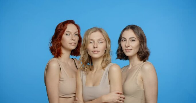 Blonde, redhead and dark haired woman are looking and smiling to the camera, portrait of different types of women in the blue screen, 4k 24p Prores