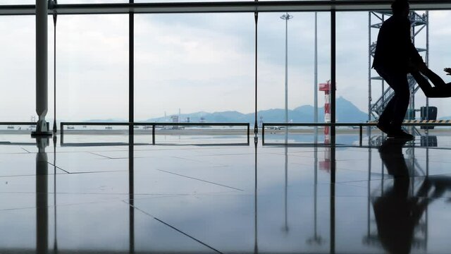 Young adult passenger couple have fun at empty terminal, recreate like children when nobody sees, woman lie ride on suitcase, man push forward. Travelers pass the time waiting for connecting flight