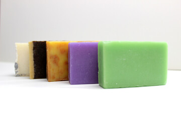 top view of various handcrafted soap with different ingredients in row on white surface.