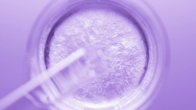 Top view macro shot of glycerin pouring into beaker with water creates ripples on its surface on violet background | Abstract body care cosmetics formulation concept