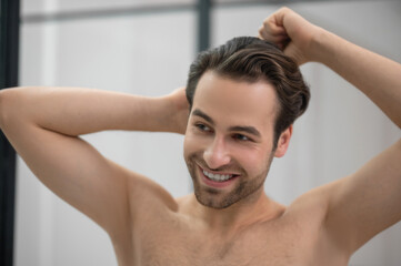 Fototapeta premium Young handsome man brushing his hair and looking contented