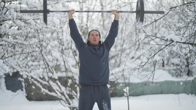 man is an sportsman, weightlifting, in the winter in the snow, raises a barbell, trains